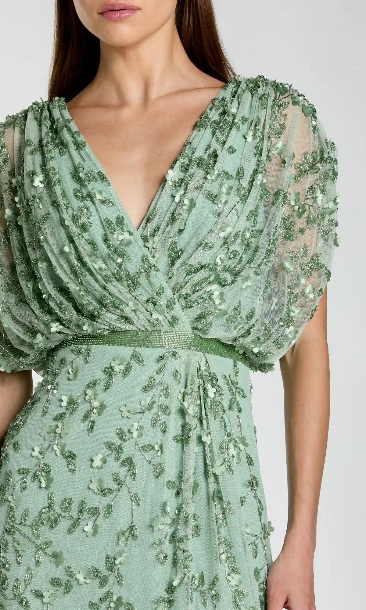 A woman models the Long Formal Dress: Mac Duggal 23067, featuring a light green sheer fabric adorned with embroidered beaded floral accents and a deep V-neckline, captured from shoulders to mid-thigh against a plain background for an elegant formal look.